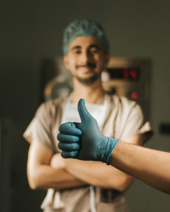 A smiling doctor in hospital scrubs giving a thumbs up, representing positive healthcare.