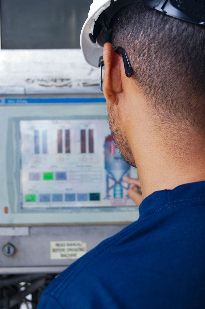 Engineer with hard hat working at an industrial control panel, displaying graphs.